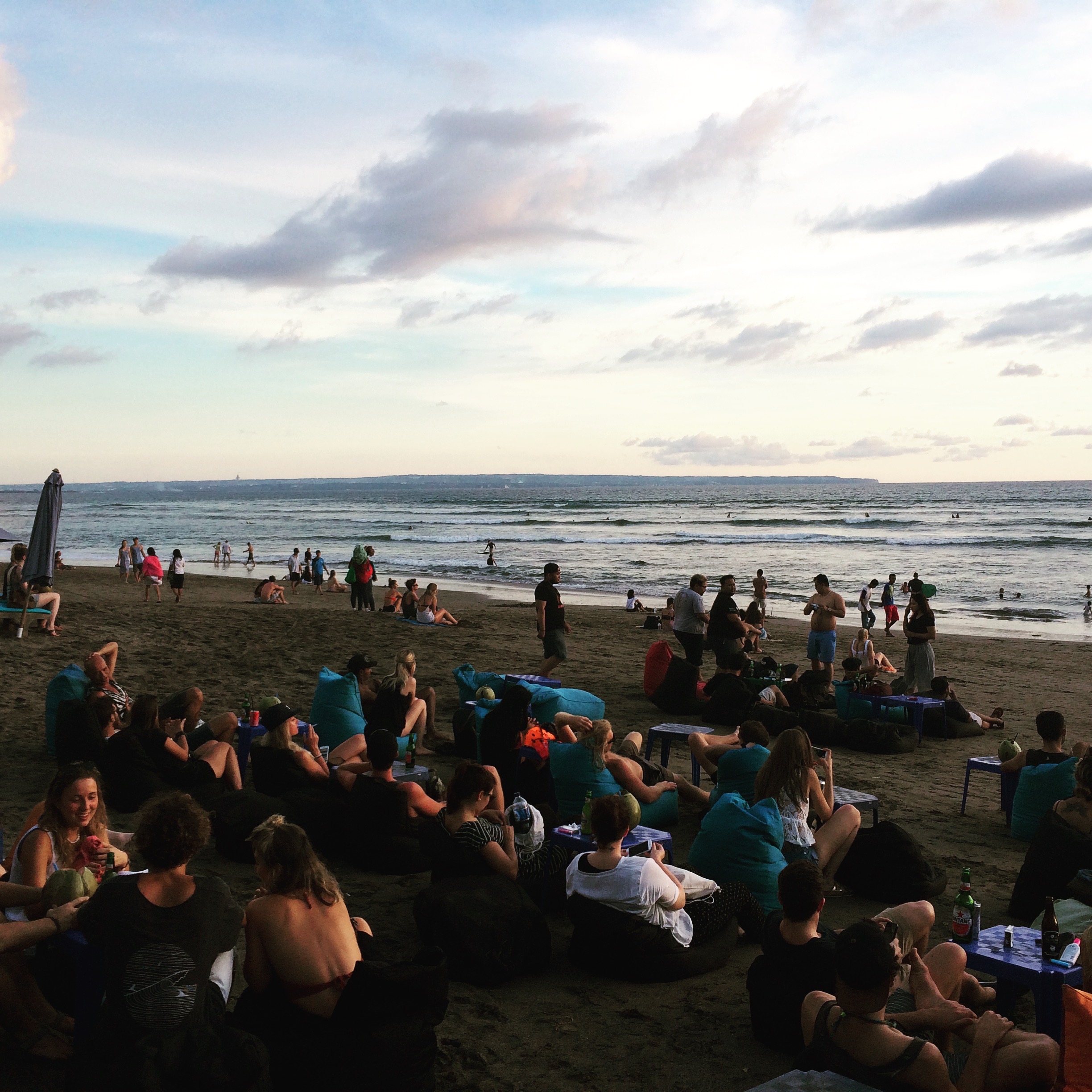 People sitting on bean bags and drinking on the beach. They are waiting for the sunset in Bali. 